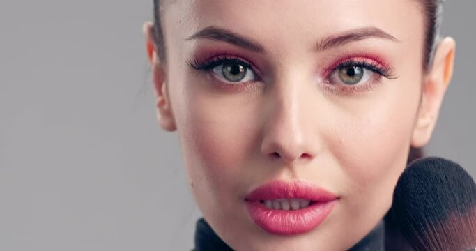 Woman makes makeup. Young woman makes  blush on the face  using makeup brush. Cosmetic concept. Beautiful brunette model doing make-up. Girl runs a makeup brush over her face.  4k Slow motion footage