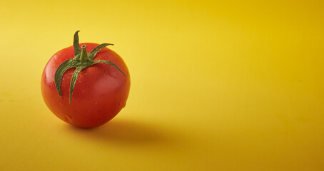 a fresh tomato with green leaves on a yellow background