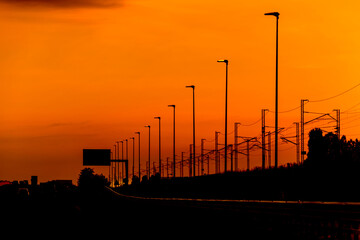 Silhouette High speed railway power line and light poles on orange sky