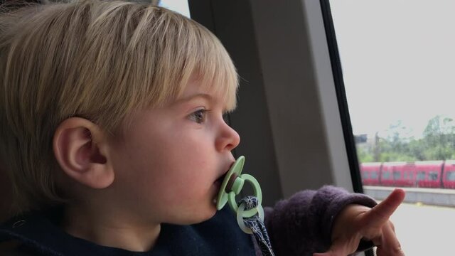 Little curious infant boy with pacifier looking interested out of a train window while driving.