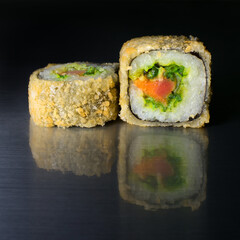Japanese roll breaded with rice, chuk and three types of fish, salmon, eel, tuna on a dark background with reflection