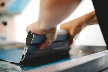 Cropped view of craftsman working on screen printing machine in designer studio  - obrazy, fototapety, plakaty