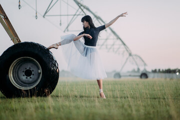 Obraz na płótnie Canvas Ballerina dances on farm near the wheel of agricultural sprayer.