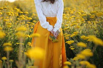 A girl in a yellow skirt and a white blouse stands in a field of yellow flowers