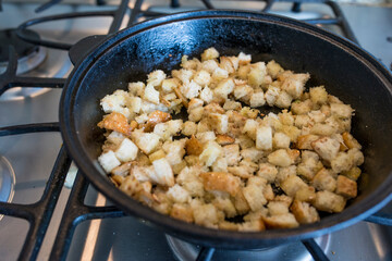 Cubed croutons frying in olive oil with garlic in cast iron skillet on gas burner stove. 