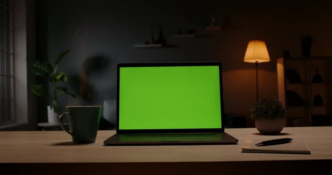 Chroma key green screen template - a laptop computer on a desk in cozy living room at night. Computer set for distance learning and remote work, technology concept 4k footage