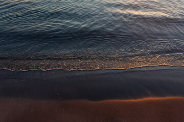 sandy beach at sunrise golden hour with calm, blue ocean and sunbeam reflection in water