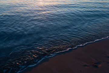 sandy beach at sunrise golden hour with calm, blue ocean and sunbeam reflection in water