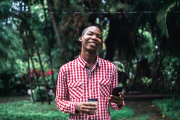 A shallow focus of a young African American male in a red and white chequered shirt using his phone in a park