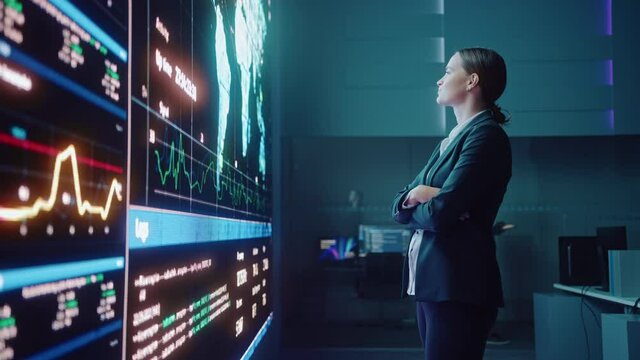 Young Female Computer Science Engineer Looking at Big Screen Display Showing Global Map with Data Points. Telecommunications Technology Company System Control and Monitoring Room with Servers.