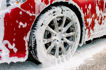 Cropped image of wheel of luxury red car in outdoors self-service car wash, covered with cleaning...