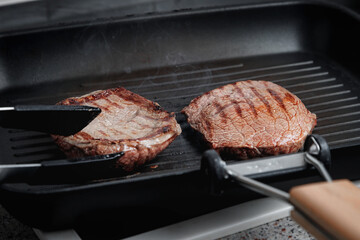 A large piece of fresh beef meat cooked in a grill pan. Stripes on the meat. Fluted frying pan.