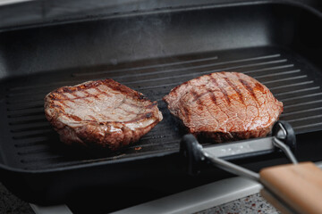 A large piece of fresh beef meat cooked in a grill pan. Stripes on the meat. Fluted frying pan.