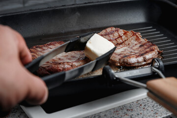 A large piece of fresh beef meat cooked in a grill pan. Meat is fried in butter. Stripes on the meat. Fluted frying pan.