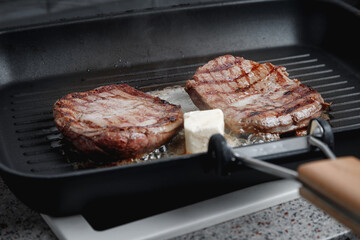 A large piece of fresh beef meat cooked in a grill pan. Meat is fried in butter. Stripes on the meat. Fluted frying pan.