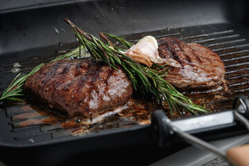 Fresh beef meat cooked on a grill pan. Meat is fried in butter. Steak with rosemary. Stripes on the meat. Fluted frying pan.