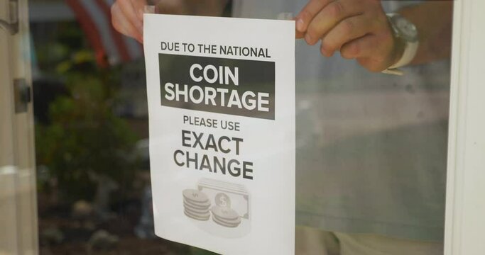 A store owner places a sign on the front window telling customers to use exact change. Coin shortages became a fact of life during the COVID-19 pandemic of 2020.	