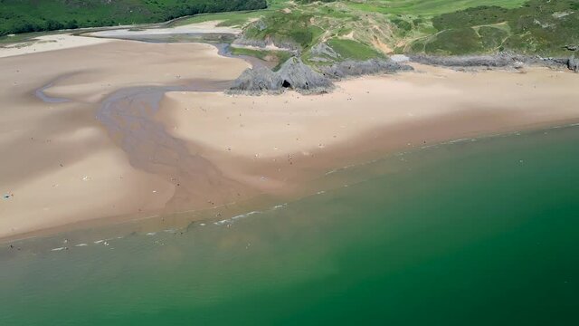 Aerial drone view of the ocean and a huge, beautiful sandy beach surrounded by cliffs (3 Cliffs Bay, Gower, Wales)