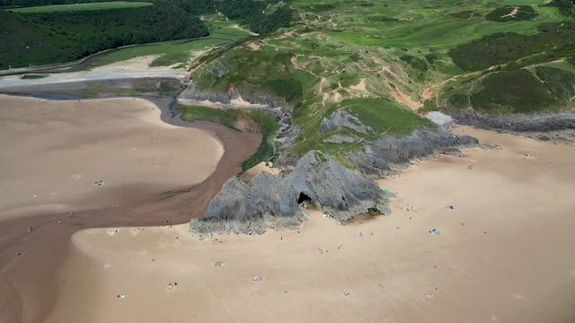 Aerial drone view orbiting distinctive cliffs on a huge sandy beach at low tide (3 cliffs and pobbles bay, Gower, Wales, UK)