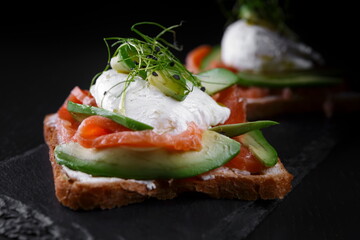 Bruschettes with salmon, avocado, cream cheese and poached egg, on a black background