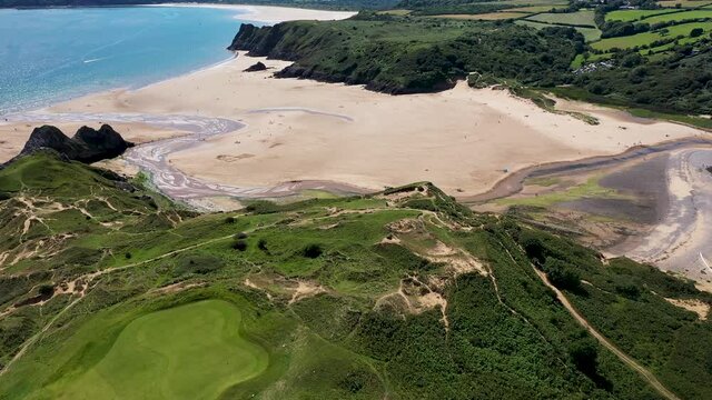 Aerial view of green foliage, large cliffs and a huge sandy beach at low tide (3 Cliffs Bay, Gower Peninsula, Wales, UK)