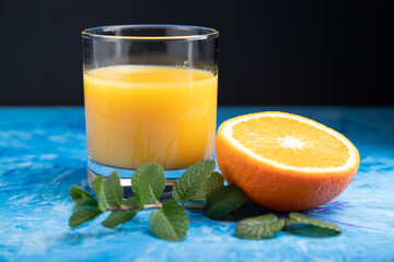 Glass of orange juice with mint on a black and blue background. Side view, close up.