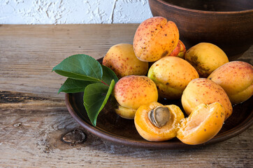 Ripe apricots with green leaves on a ceramic plate on a wooden table.