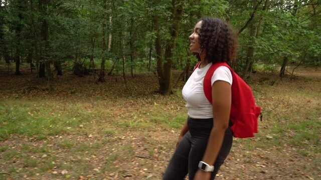 Teenage mixed race African American girl young woman hiking with a red backpack and wearing a smart watch in forest woodland 