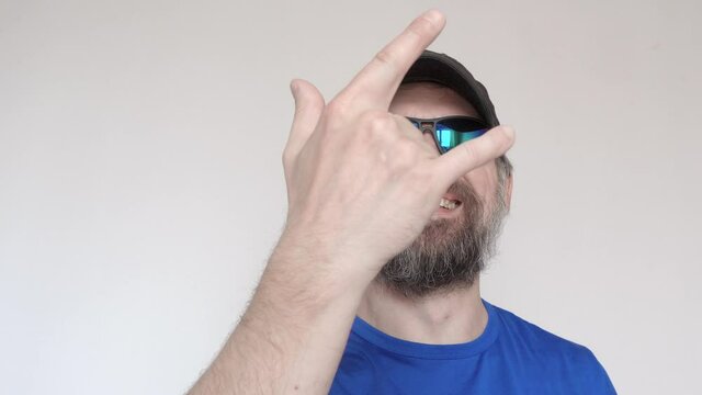 Adult man in blue t-shirt and sunglasses shows rock gesture and smiles.