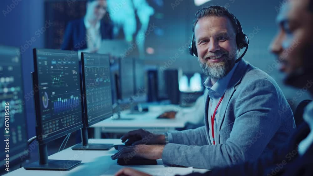 Wall mural bearded happy senior technical support specialist is talking on a headset while working on a compute