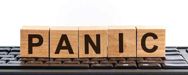 PANIC word made with building blocks. A row of wooden cubes with a word written in black font is located on a black keyboard
