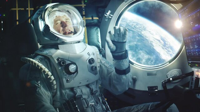 Portrait of a Happy Astronaut on a Space Ship In Orbit. Cosmonaut in a Futuristic Suit is Full of Joy and is Waving Hand on a Video Call. VFX Graphics Footage from the International Space Station.