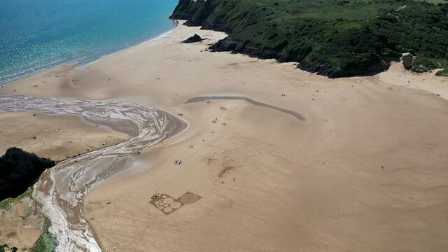 Aerial view of green foliage, large cliffs and a huge sandy beach at low tide (3 Cliffs Bay, Gower Peninsula, Wales, UK)