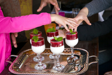 Hands stretch  to  glasses with raspberry panna cotta, which is decorated with mint leaves.