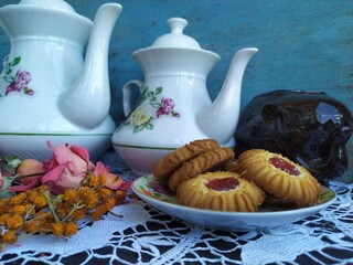 Kitchen still life white tea pot glass with cup holder cookies dry roses on the lace tablecloth on a wooden table
