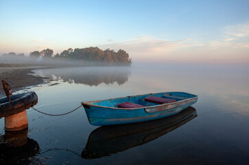 Early, foggy morning on the lake. A lone boat at the shore.