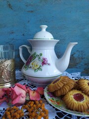 Kitchen still life white tea pot glass with cup holder cookies dry roses on the lace tablecloth on a wooden table