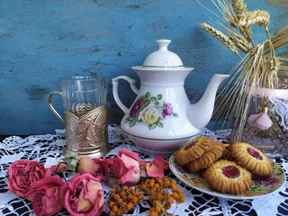 Kitchen still life white tea pot glass with cup holder cookies dry roses on the lace tablecloth on a wooden table