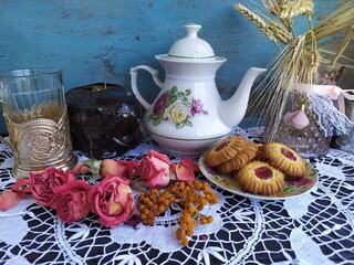 Kitchen still life white tea pot glass with cup holder cookies dry roses on the lace tablecloth on a wooden table