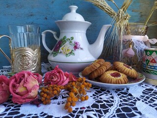 Kitchen still life white tea pot glass with cup holder cookies dry roses on the lace tablecloth on a wooden table