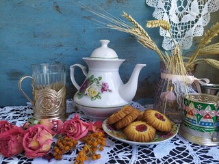 Kitchen still life white tea pot glass with cup holder cookies dry roses on the lace tablecloth on a wooden table