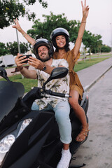 Cheerful Stylish Couple Satting On Modern Motorbike Outdoors and making a selfie with a smartphone
