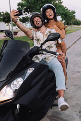 Fototapeta na wymiar Cheerful Stylish Couple Satting On Modern Motorbike Outdoors and making a selfie with a smartphone