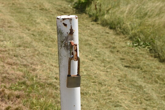 Old Rusty Padlock Locked On White Painted Pillar Of The Entrance Gate To The Field Road.