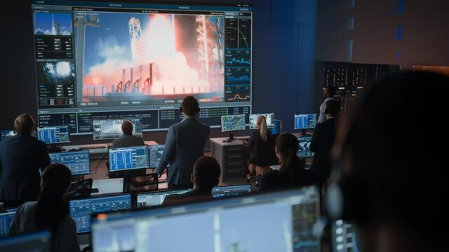 Group of People in Mission Control Center Witness Successful Space Rocket Launch. Flight Control Employees Sit in Front Computer Displays and Monitor the Crewed Mission. Team Stand Up and Clap Hands.