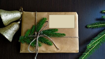 a christmas gift wrapped in craft paper and tied with linen thread with a mock-up next to fir branches and golden bells