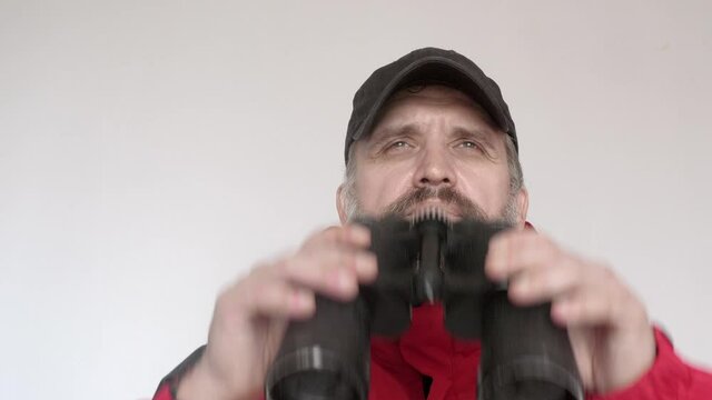 Man in red coad looks ahead through binoculars. Watching faraway objects.
