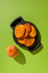 Healthy sweets. Dried whole peaches on a wooden serving plate. Fresh ripe peach lies nearby. Top view, copy space