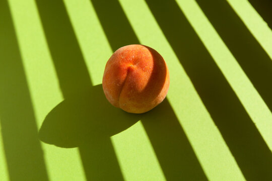 Beautiful ripe peach on a light green background with striped shadows of sunlight