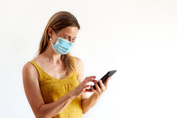 Woman wearing face protective mask looking at her mobile phone texting during virus outbreak quarantine - woman isolated on white background using mobile phone